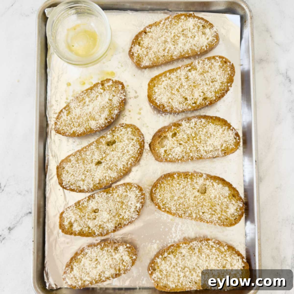 Slices of crusty gluten-free bread on a foil-lined tray, freshly sprinkled with finely grated Parmesan cheese, ready for the broiler.