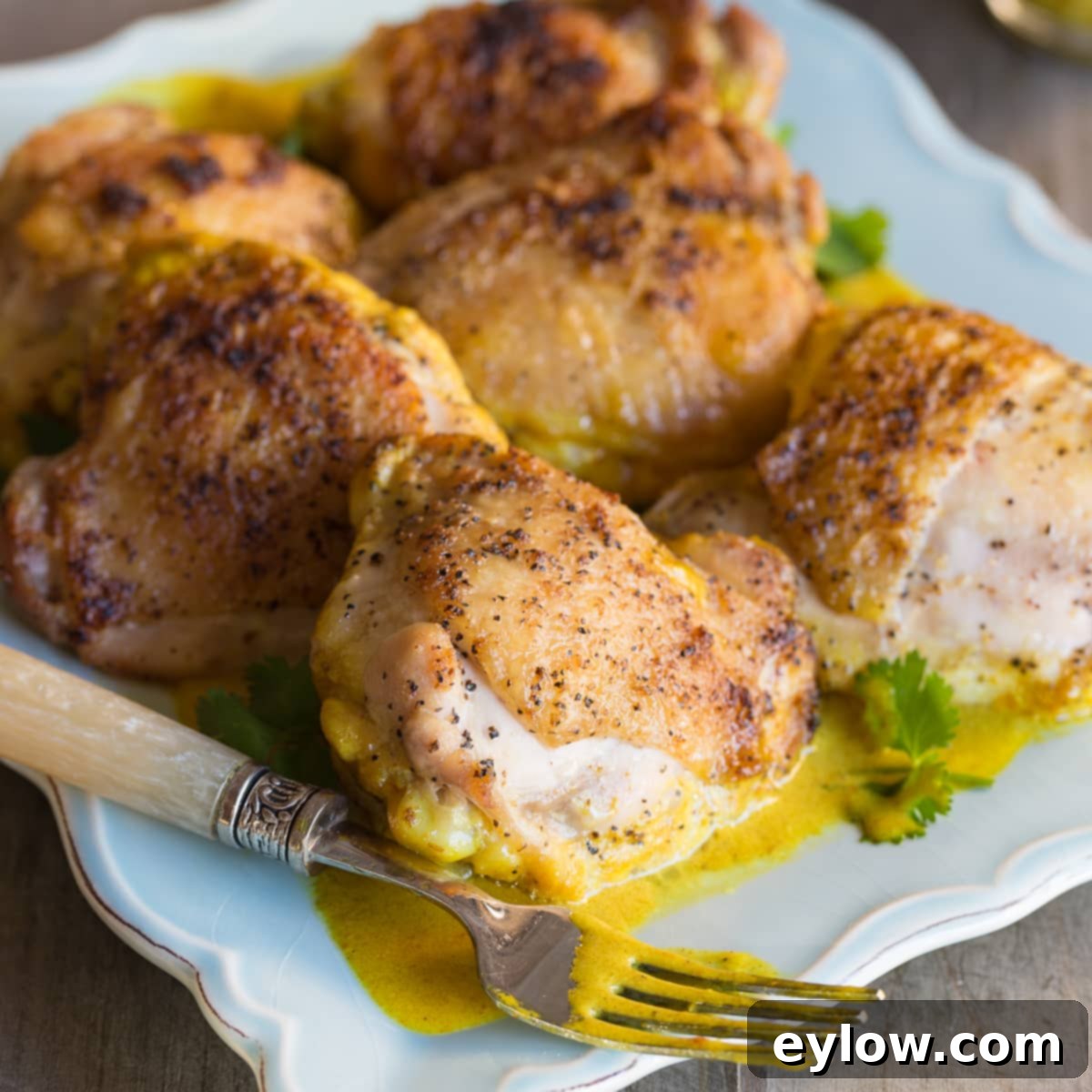A blue plate with golden chicken thighs and bright yellow curry sauce. 