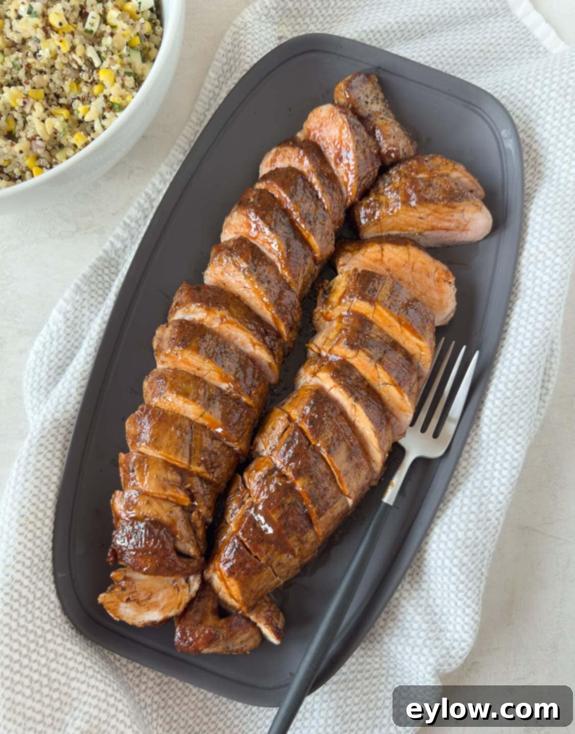 Pellet Grill Smoked Pork Tenderloin 2 Sliced pork tenderloins glazed with bbq sauce on a gray platter with a salad beside.