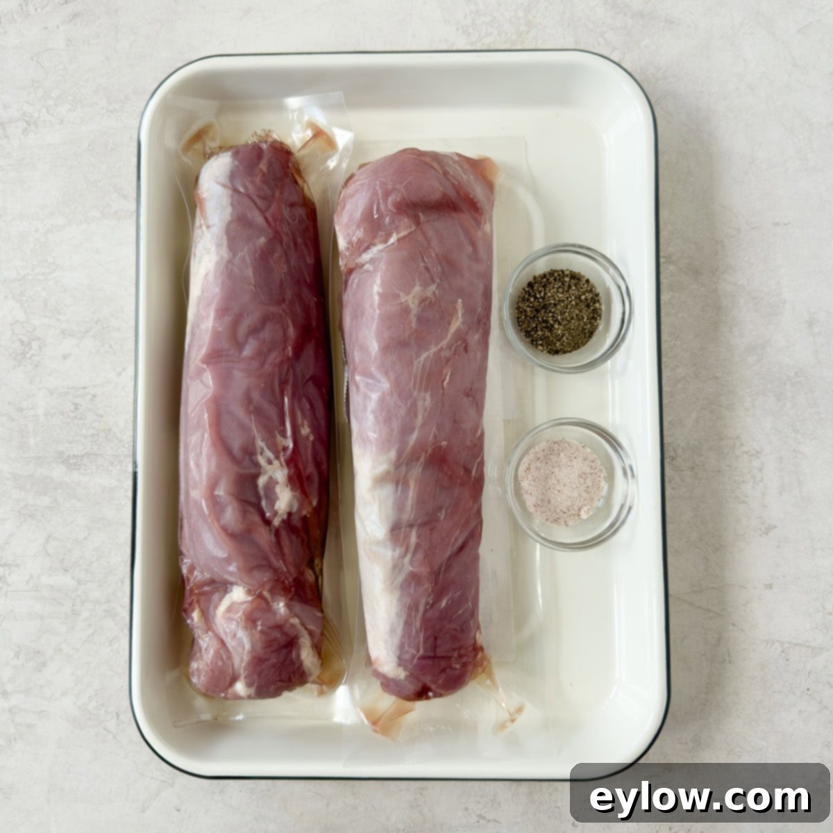 Pellet Grill Smoked Pork Tenderloin 3 Raw pink pork tenderloins on a white tray with small bowls of salt and pepper to season.
