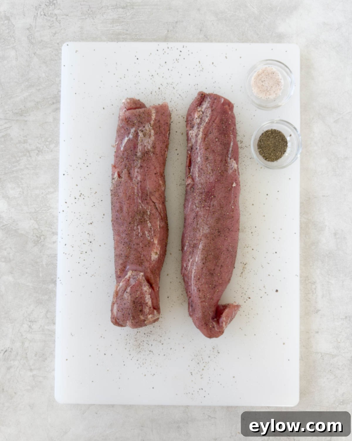 Pellet Grill Smoked Pork Tenderloin 5 Pork tenderloin being seasoned with salt and pepper on a white cutting board.