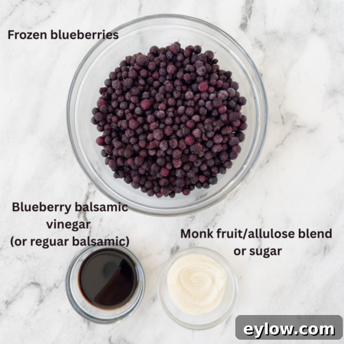 Effortless Blueberry Compote 3 A glass bowl holds a mound of vibrant frozen blueberries, flanked by a small bowl of granulated sugar and a bottle of rich balsamic vinegar, key ingredients for this compote recipe.