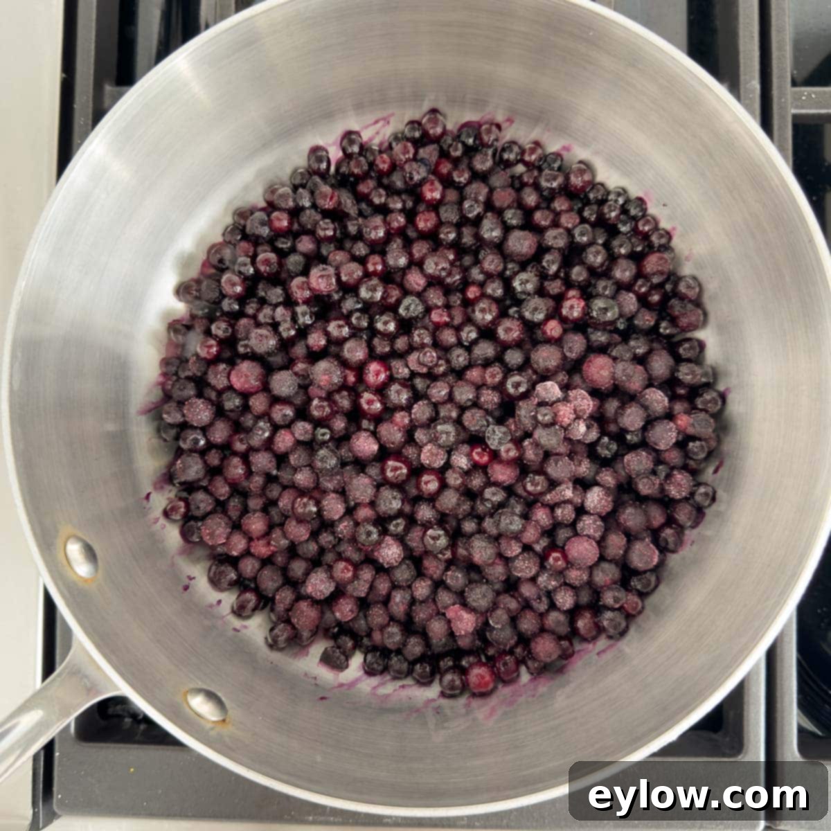 Effortless Blueberry Compote 4 A sturdy stainless steel pan sits on a stovetop, filled with a generous amount of glistening frozen blueberries, ready for cooking.