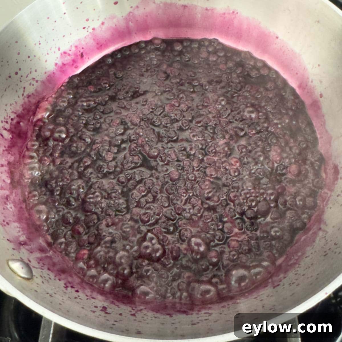 Effortless Blueberry Compote 6 Lush blueberries are actively bubbling and simmering in a pot on the stovetop, their juices reducing and thickening into a delicious compote.