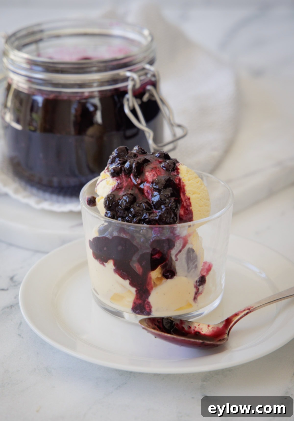Effortless Blueberry Compote 9 A clear glass cup of creamy vanilla ice cream is generously topped with a rich, vibrant purple blueberry compote, creating a delightful dessert.
