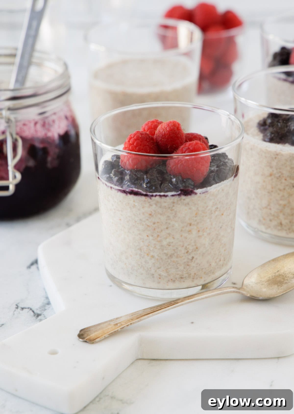 Glasses of chia pudding with coconut milk topped with blueberries and raspberries.