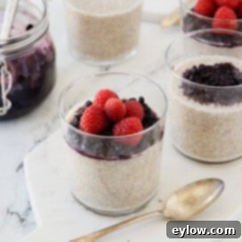A glass of cream chia coconut pudding topped with blueberries and raspberries with a silver spoon.