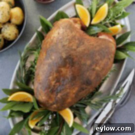 A browned, whole smoked turkey breast in a silver platter with bay leaves, potatoes on side,