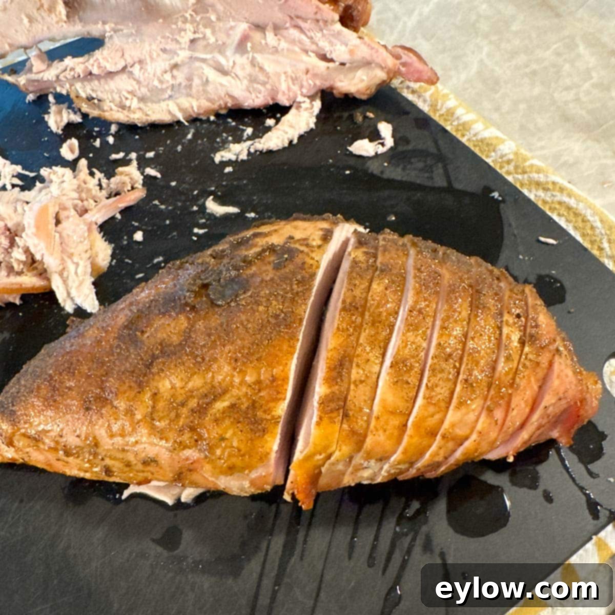 Half of a smoked turkey breast sliced on a black cutting board.