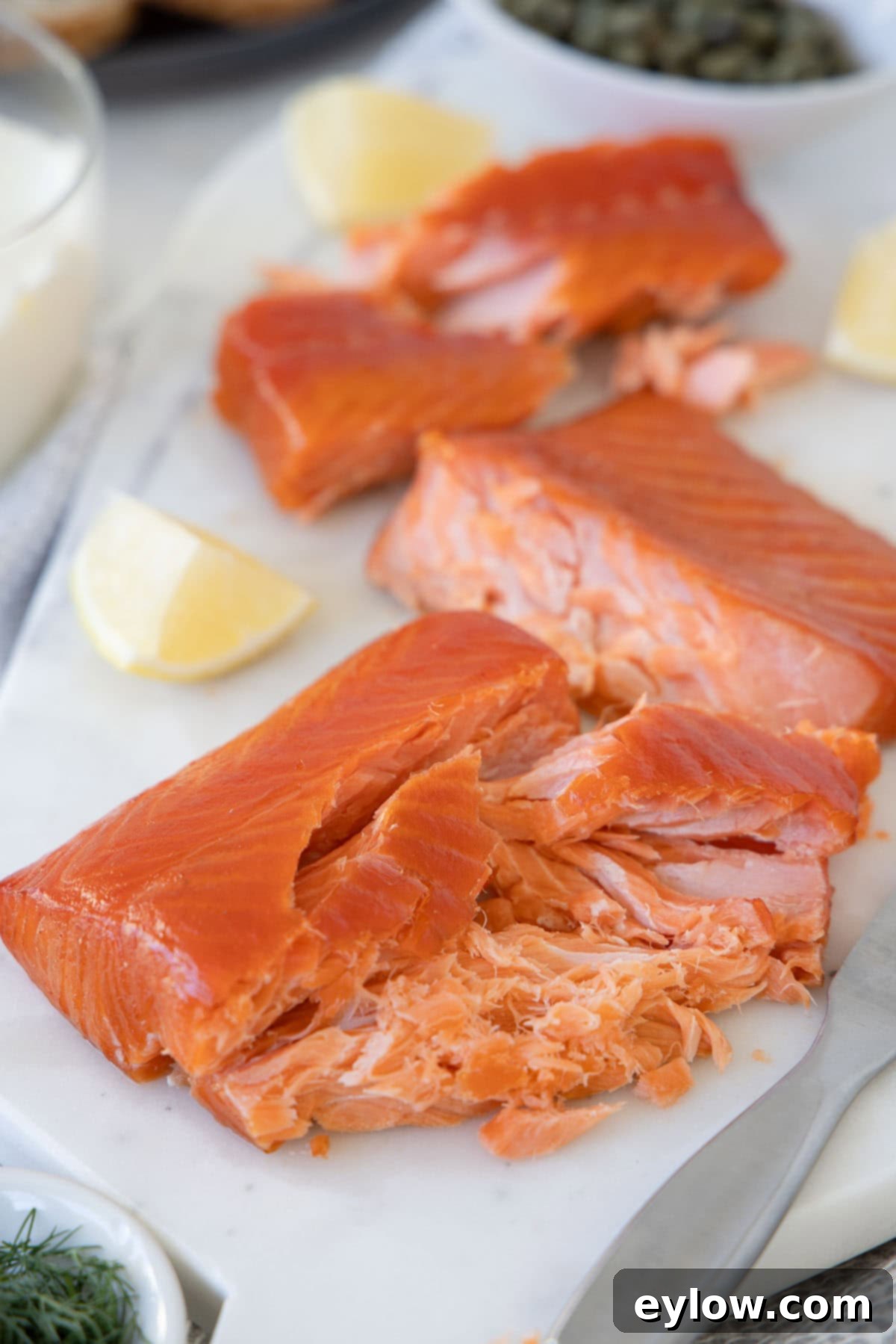 Pellet Grill Smoked Salmon Perfection 2 Bright orange smoked salmon chunks on a white board with lemon wedges and capers in the back.
