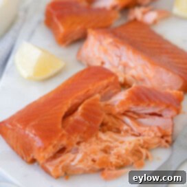 Flaked smoked salmon from a pellet grill on a serving board with lemons.