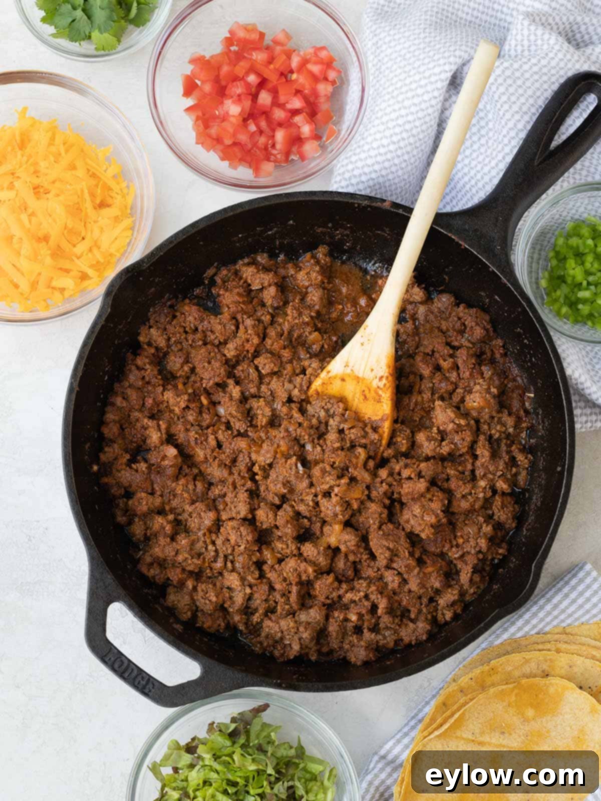 Savory spiced taco meat in a black cast iron skillet ready for tacos, garnished with fresh cilantro and a lime wedge.