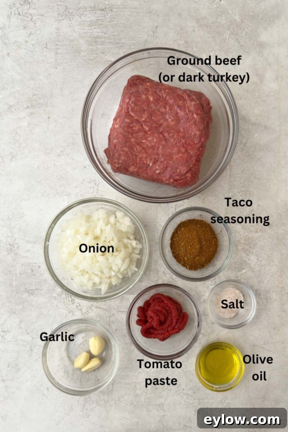 Simple, fresh ingredients laid out for making ground taco meat including ground beef, onion, garlic, tomato paste, and spices.