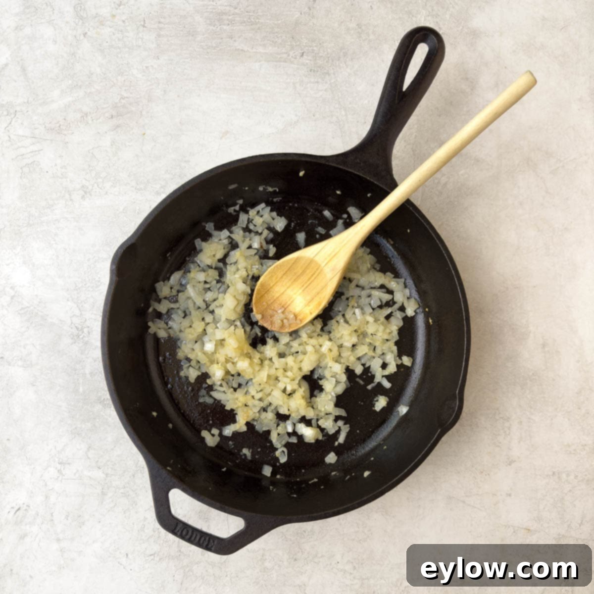 Chopped onions sautéing in olive oil in a black cast iron skillet until soft and translucent.