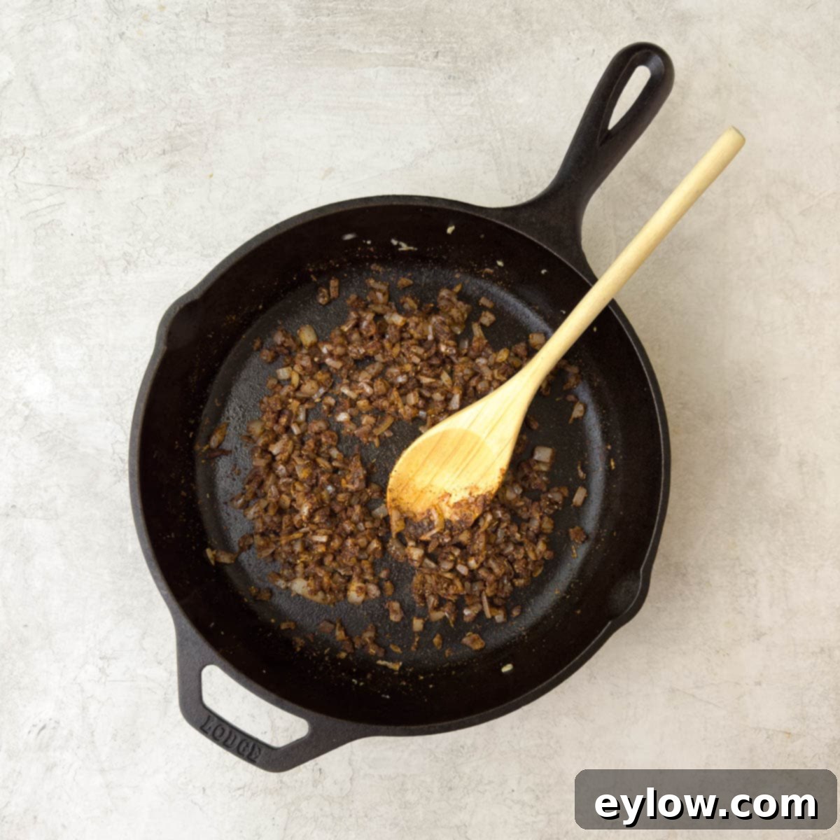Adding taco seasoning blend and a tablespoon of water to the cooked onions and garlic in the skillet.