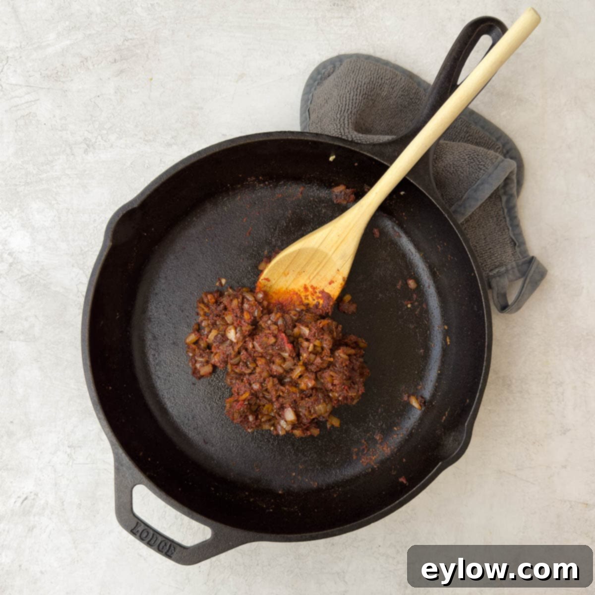 Tomato paste being added to the spices and onions in the pan, ready to be stirred in.