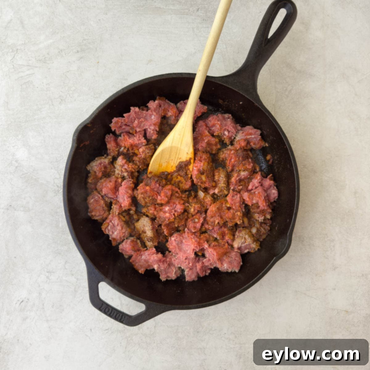 Ground beef being added to the seasoned onion and tomato paste mixture in the skillet.