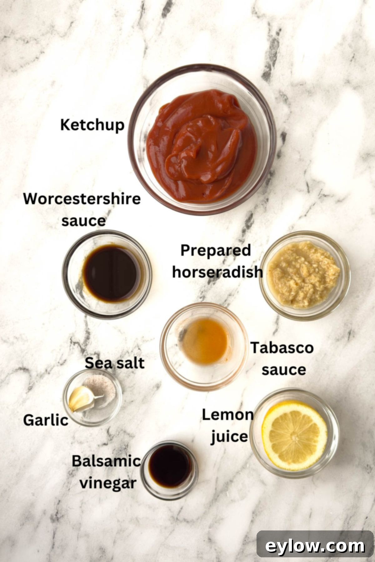 Individual bowls holding ingredients for homemade cocktail sauce: ketchup, horseradish, lemon, garlic, Worcestershire, and balsamic vinegar.