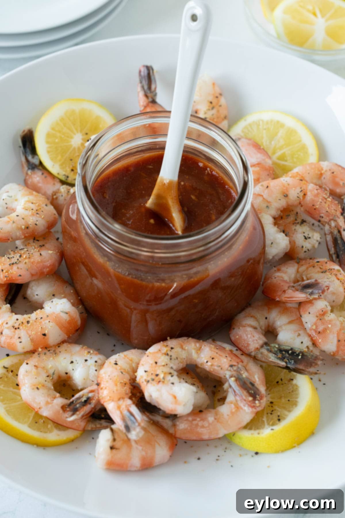A beautiful appetizer presentation of cooked shrimp in a bowl with lemon slices, featuring a jar of cocktail sauce in the center.