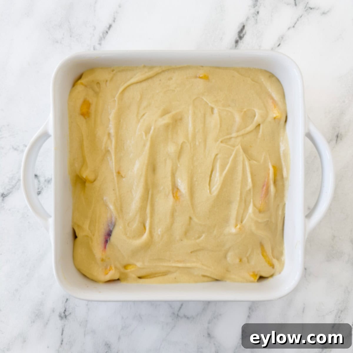 A white baking dish spread over the top with creamy batter for a cobbler. 