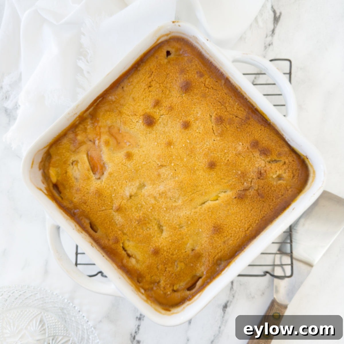A baked peach cobbler with a golden crusty top on a cooling rack.