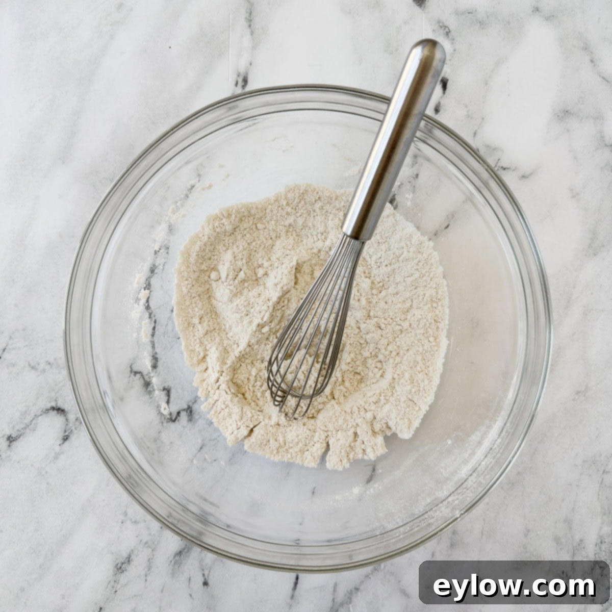 A glass bowl of flour and dry ingredients for baking a cobbler.