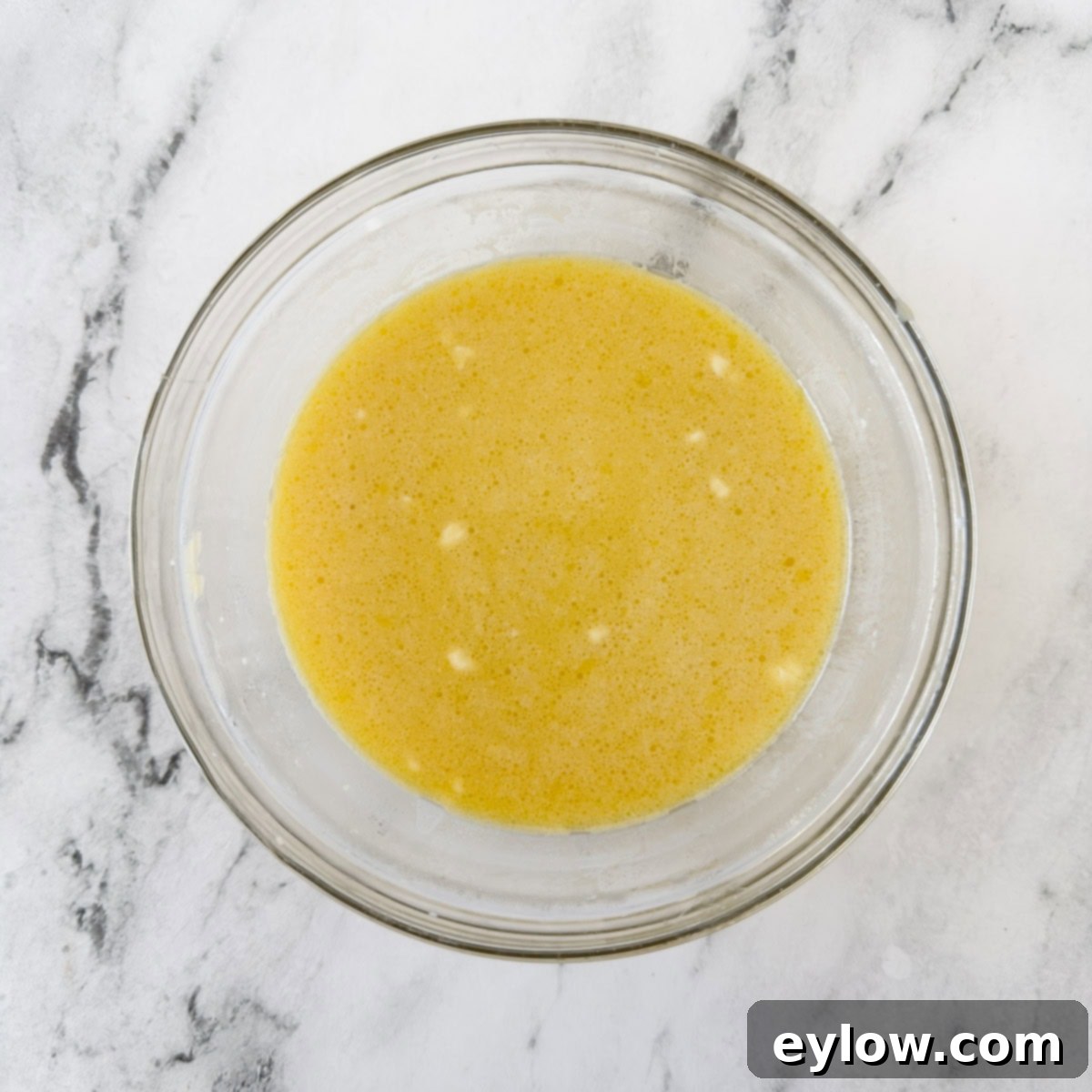 A glass bowl of eggs, milk and melted butter.