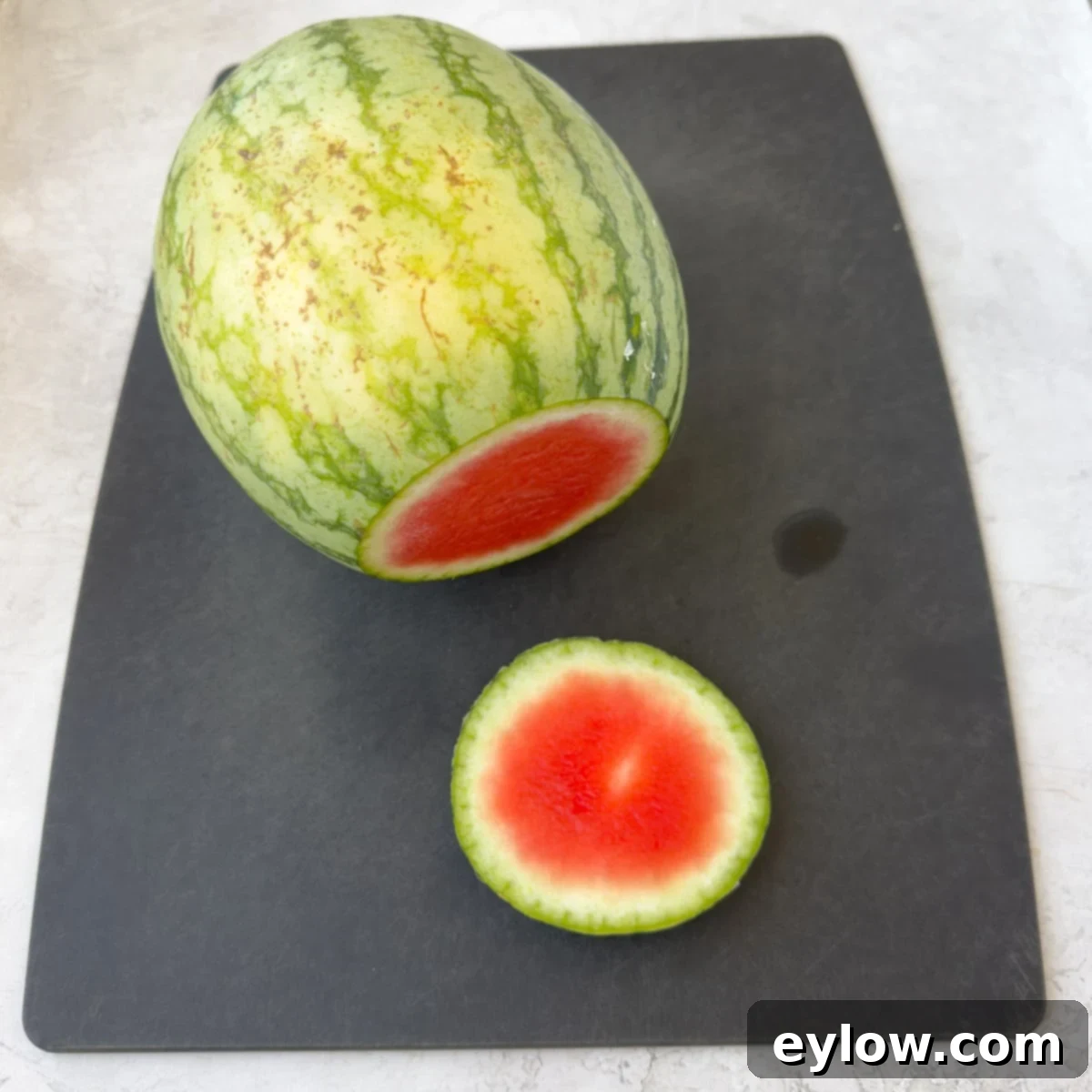 A mini seedless watermelon on a cutting board.