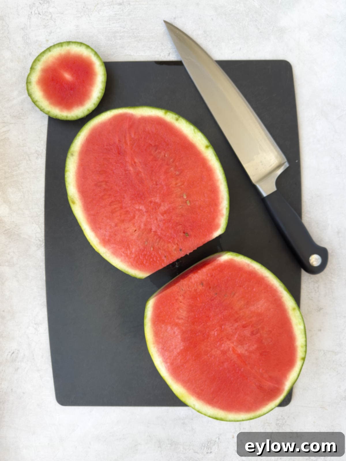 Red seedless watermelon cut on half on a black cutting board.