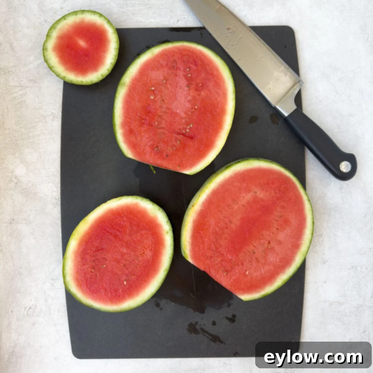 Big slices of red watermelon on a black cutting board with knife.