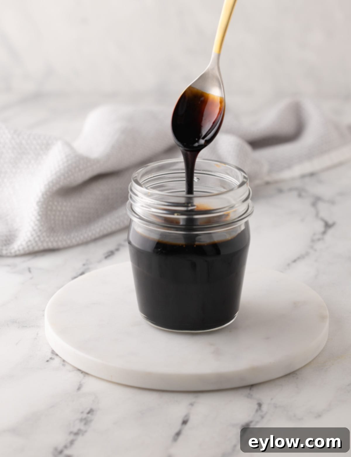 Homemade Balsamic Glazed Strawberries 6 Molasses colored balsamic glaze in a jar dripping off spoon.