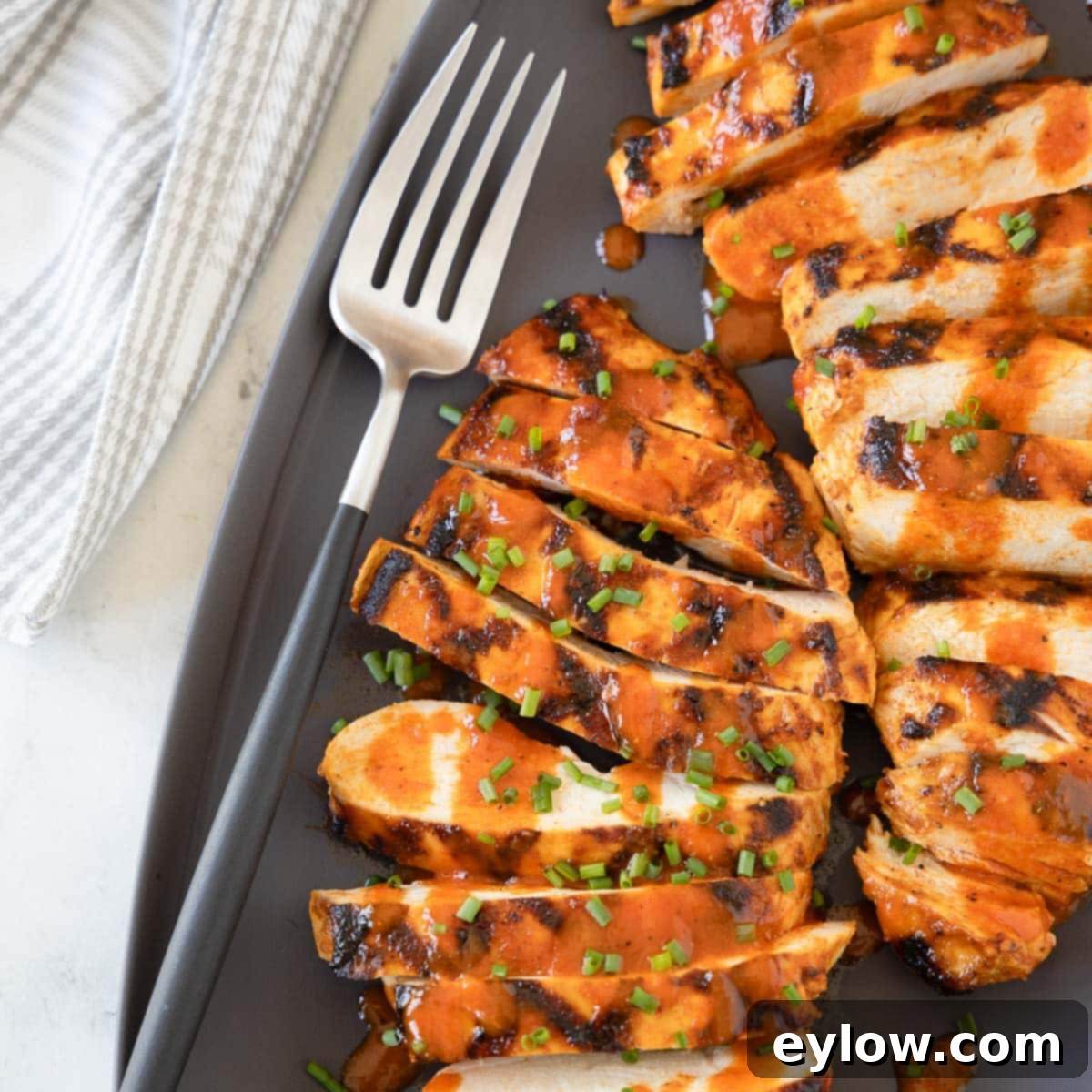 Bright red orange Buffalo grilled chicken breasts on a gray platter with a serving fork.