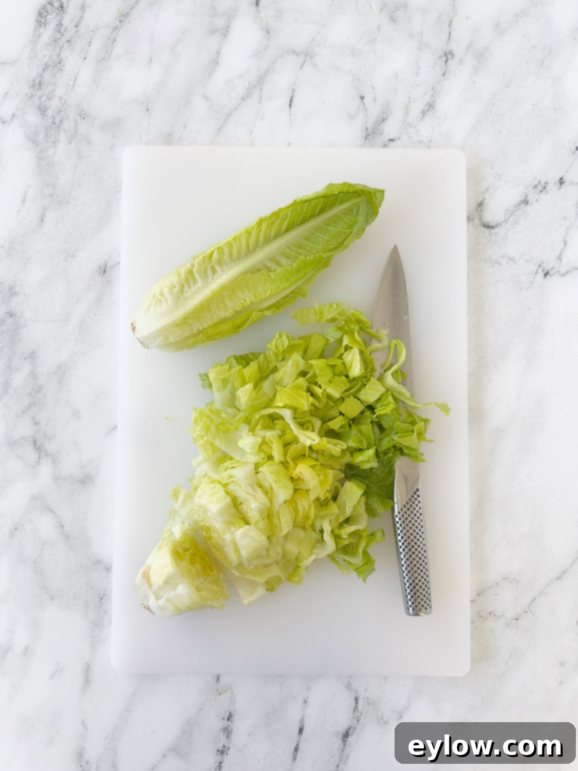 Chopping hearts of Romaine lettuce on a cutting board with a chef's knife.