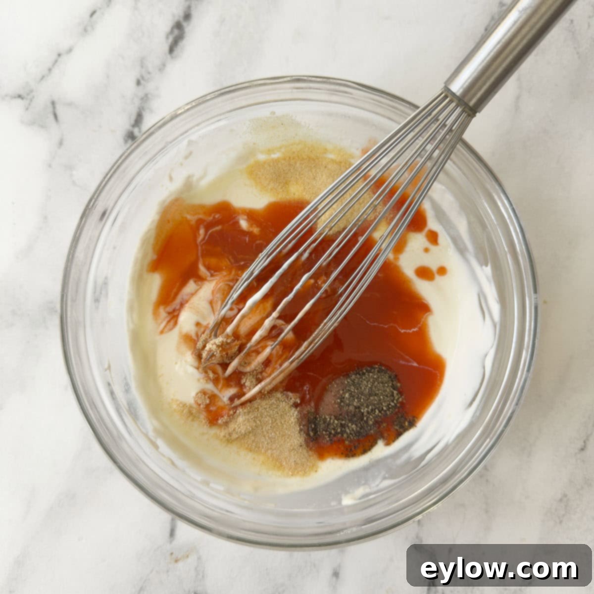 Blending ingredients for buffalo ranch dressing in a glass bowl with a whisk.