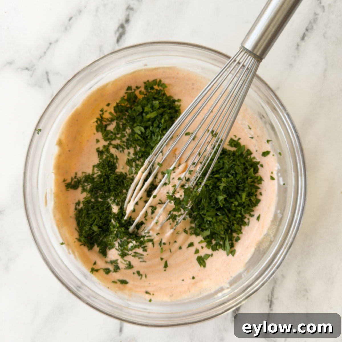 Adding fresh chopped green herbs to a bowl of buffalo ranch dip.