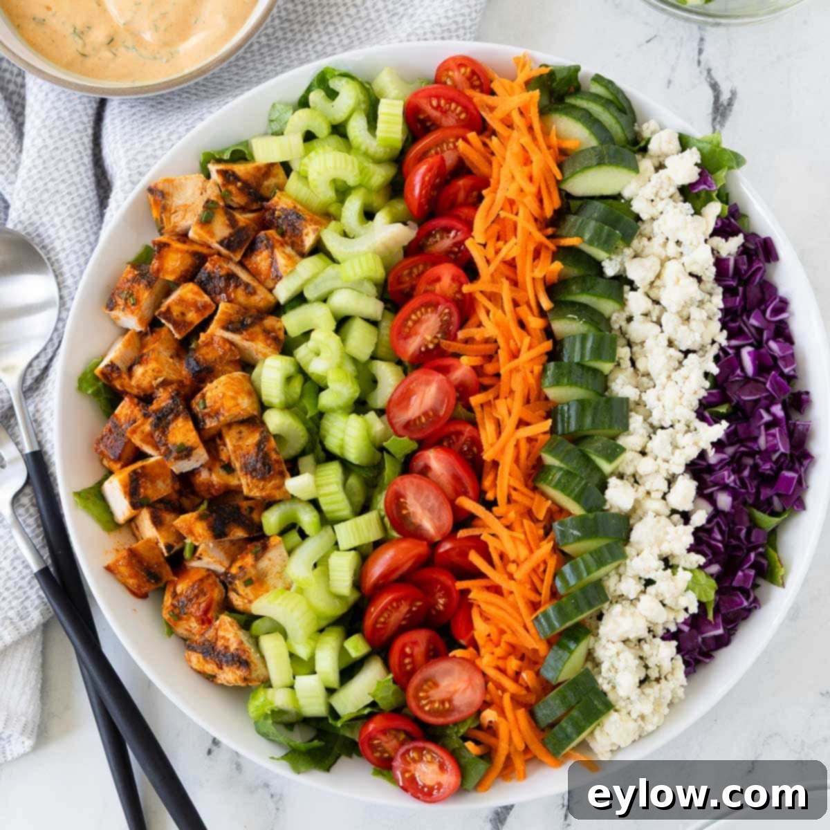 Colorful rows of buffalo chicken salad in a round bowl with creamy dressing on the side.