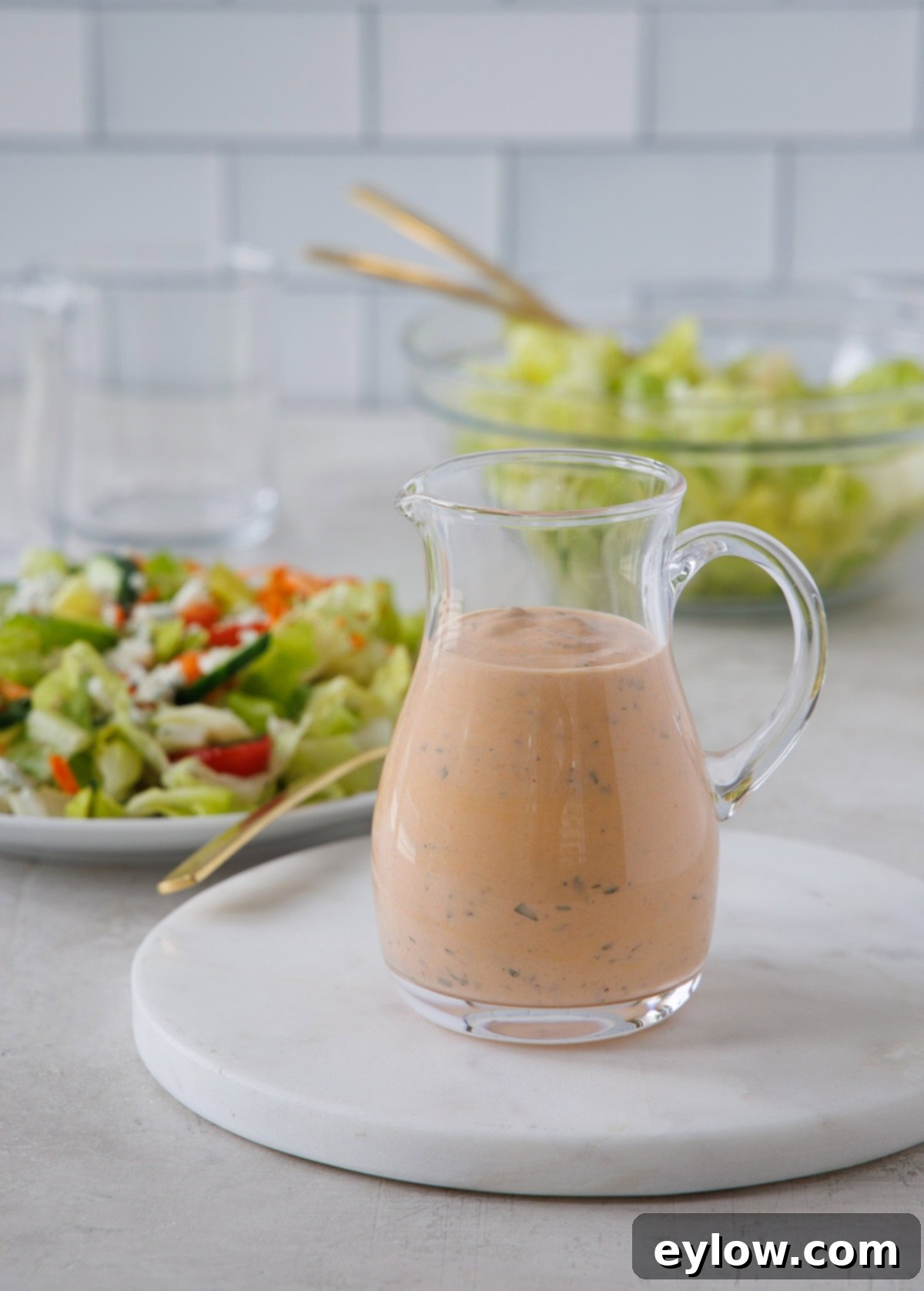 A glass cruet of creamy orange buffalo ranch dressing with a salad near by.