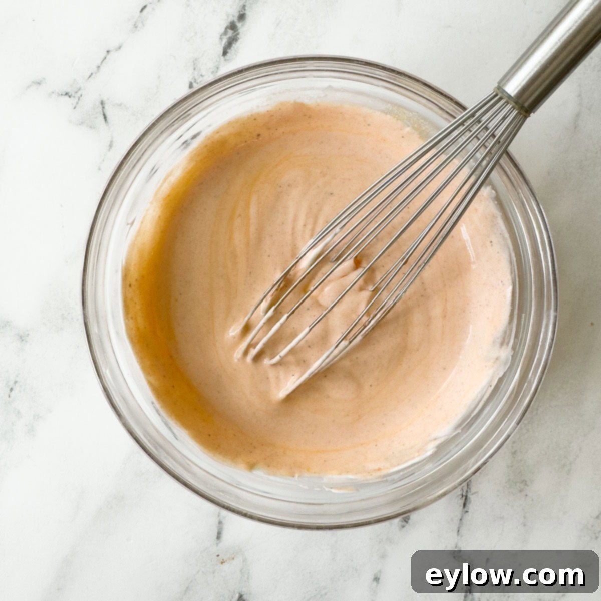 Creamy light orange buffalo dressing being made in a bowl with a whisk.