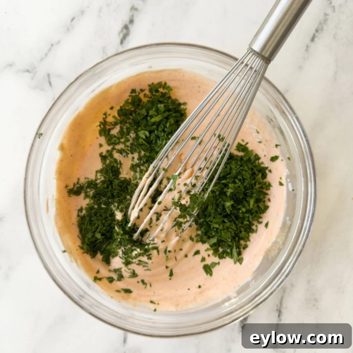 Adding fresh chopped green herbs to a bowl of buffalo ranch dip.
