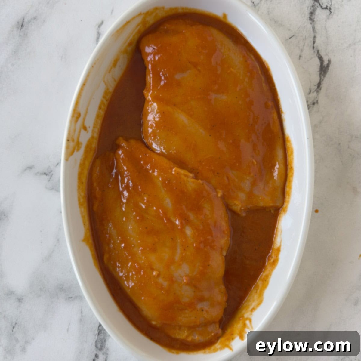 Zesty Grilled Buffalo Chicken 6 Boneless chicken breasts marinating in an oval white shallow dish.