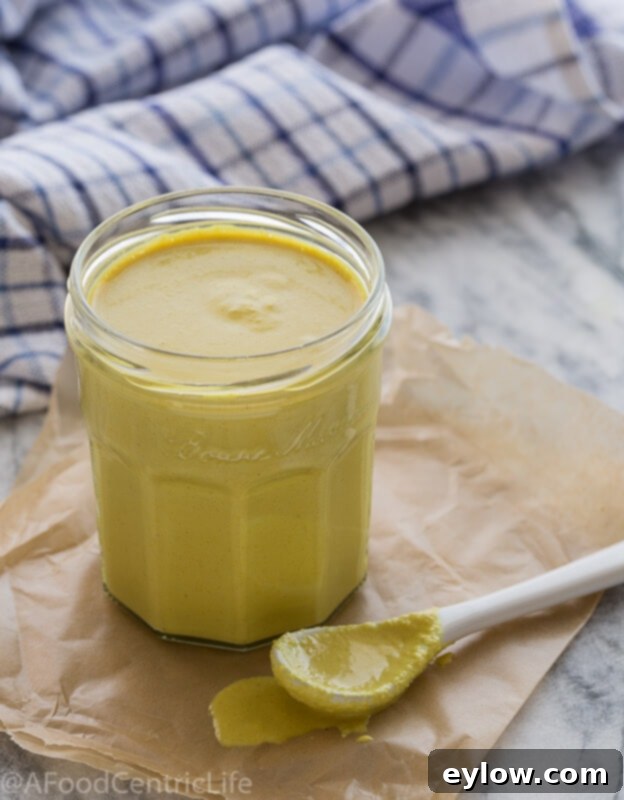 Velvety Plant Cheese Sauce 2 Vegan cheese sauce in a jar with a white spoon on a table, ready to be served.