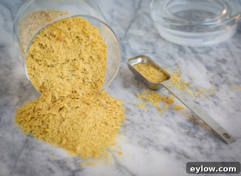 nutritional yeast | AFoodCentricLife.com Golden nutritional yeast flakes spilled on a counter with a measuring tablespoon, illustrating the key ingredient for vegan cheese sauce.