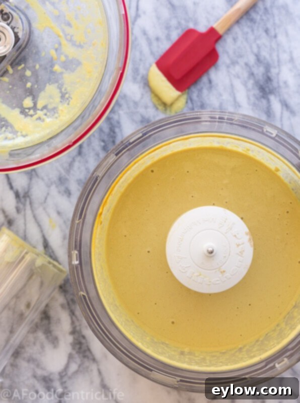 vegan cheese sauce | AFoodCentricLife.com Golden vegan cheese sauce being blended in a food processor bowl, showing its creamy texture.