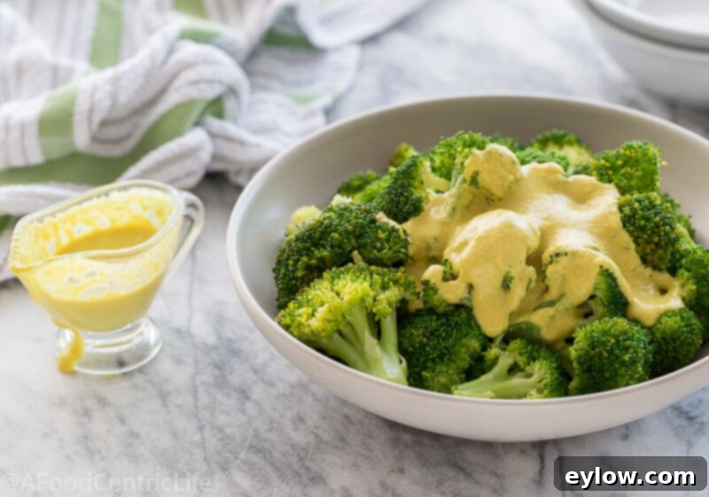 vegan cheese sauce | AFoodCentricLife.com Creamy vegan cheese sauce drizzled generously over bright green steamed broccoli in a white bowl.