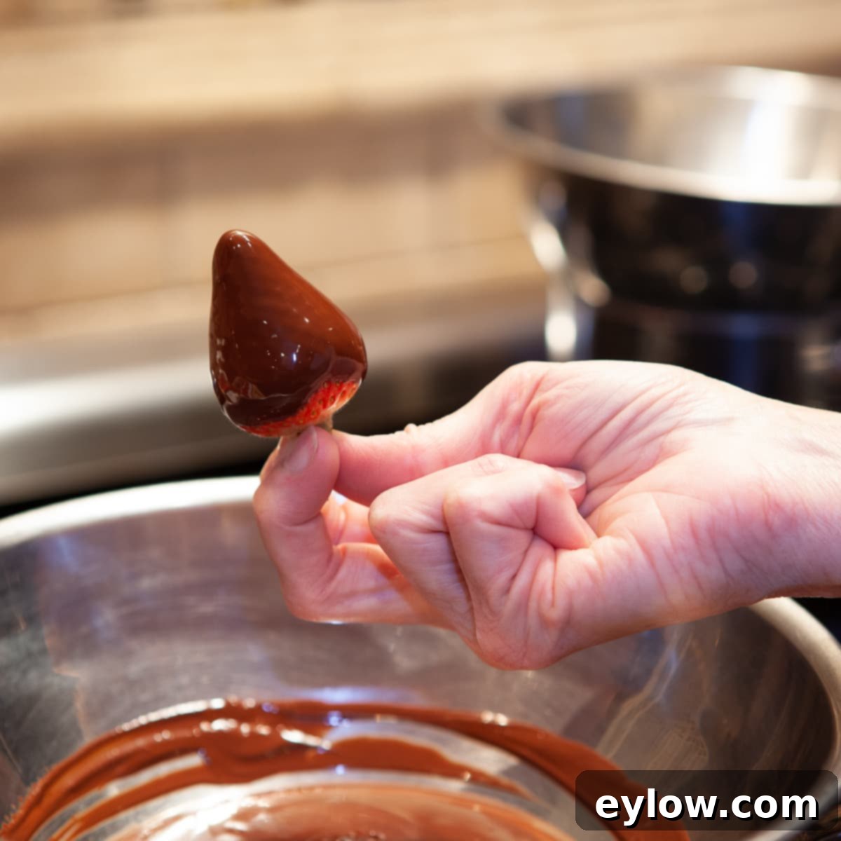 Chocolate Dipped Strawberries Technique A single perfectly chocolate-dipped strawberry suspended over a bowl of melted chocolate, showcasing its flawless coating.