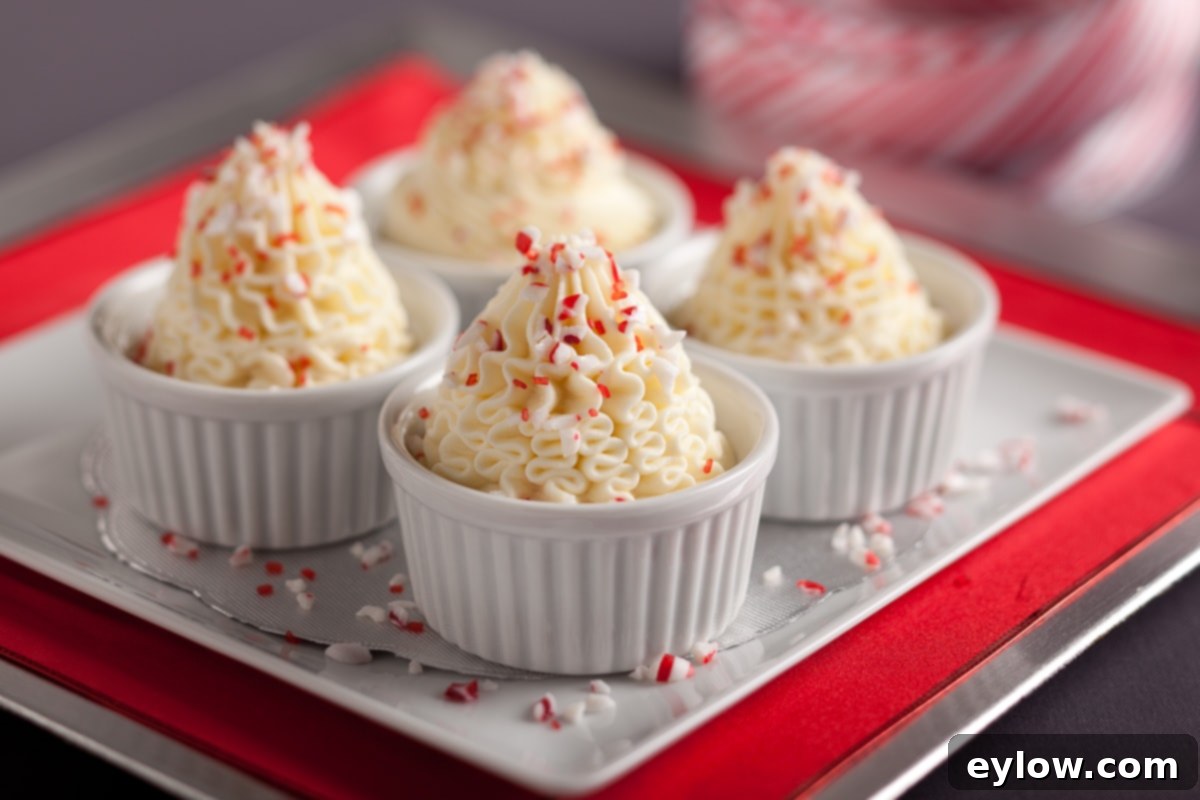 Four white ramekins of white chocolate mousse topped with crushed peppermint candy garnish on a tray.