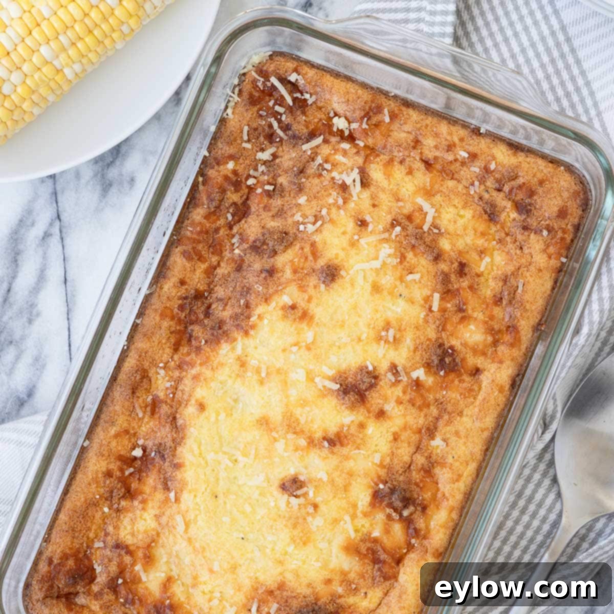 Golden corn souffle, right out of the oven in a glass baking dish on a gray plaid kitchen towel.