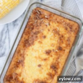 Golden corn souffle in a glass baking dish on a gray plaid kitchen towel.