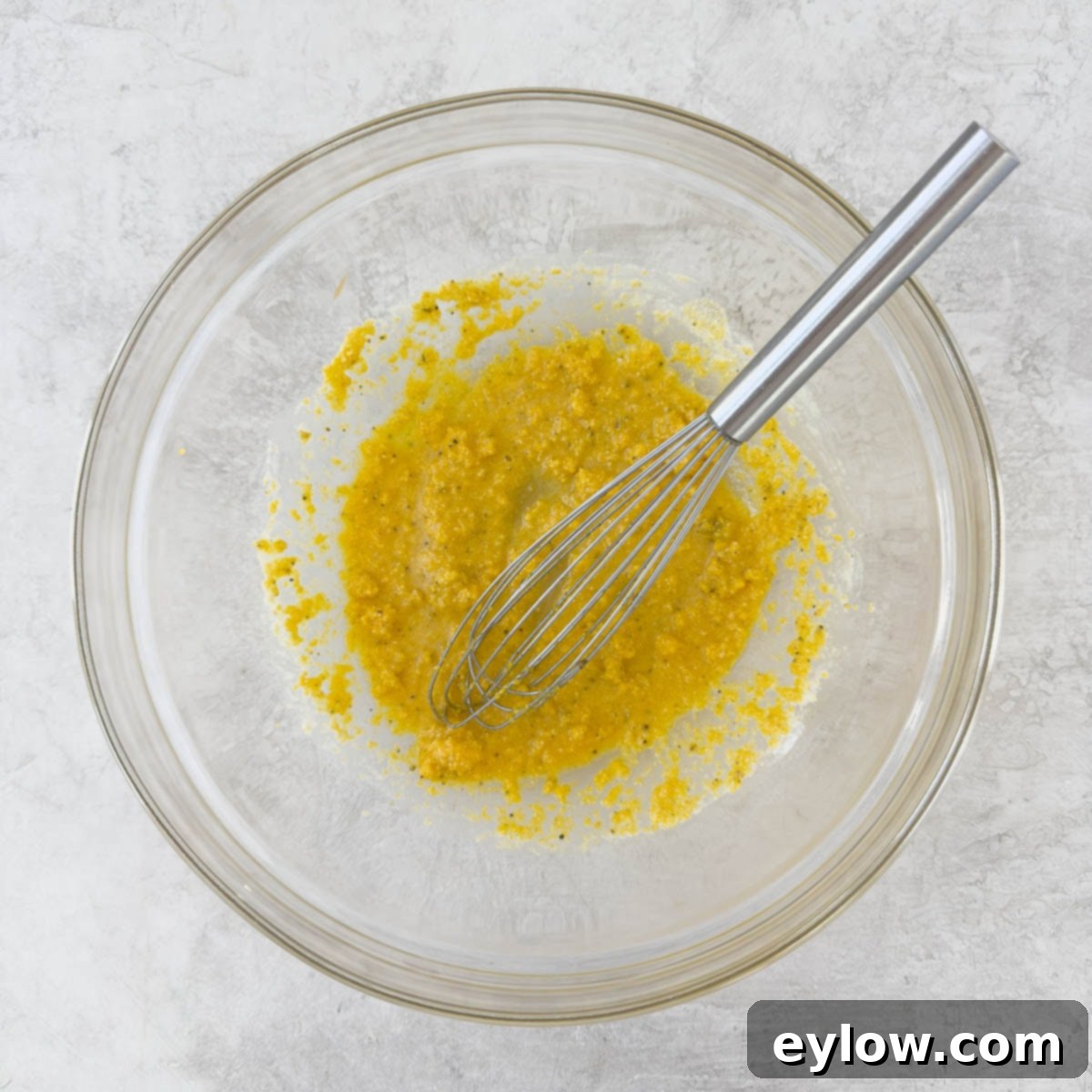 Glass bowl with cornmeal and silver whisked being mixed.