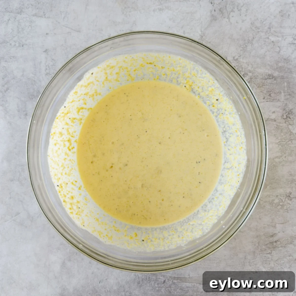 A bowl of corn souffle batter with corn kernels and half and half.
